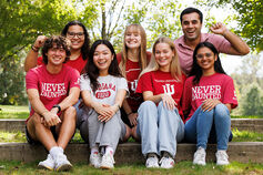 A male student in an IU sweatshirt talks with another person across a desk.